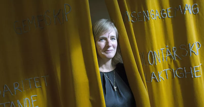 Marika Markovits är chef för Stockholms Stadsmission. Marika Markovits kikar fram mellan gula drapperier.