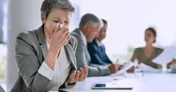 En kvinna nyser i ett mötesrum. 