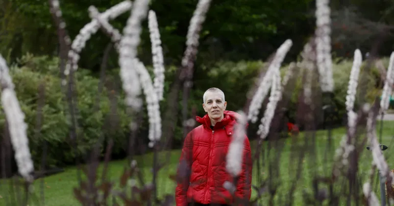 Maria Westin  Maria Westin i röd jacka, hon står på avstånd i förgrunden svajar några vita växter.