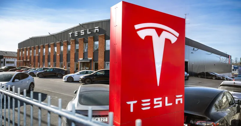 Tesla sympatitåtgärd Unionen varslar om ny blockad mot Tesla – WAECO förbjuds utföra arbete från 3 november. Facklig kamp fortsätter för kollektivavtal. En röd Tesla-skylt i fronten mot en byggnad i bakgrunden