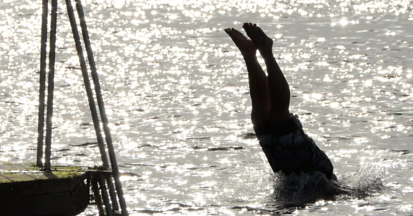 Semestertiderna närmar sig med stormsteg - snart är det dags för sol och bad. Person dyker i vatten från brygga.