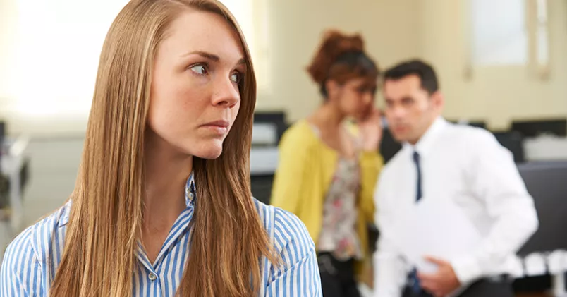 Mobbning på jobbet ökar och det är chefer som mobbar mest. Kvinna sneglar bakåt mot personer som viskar.