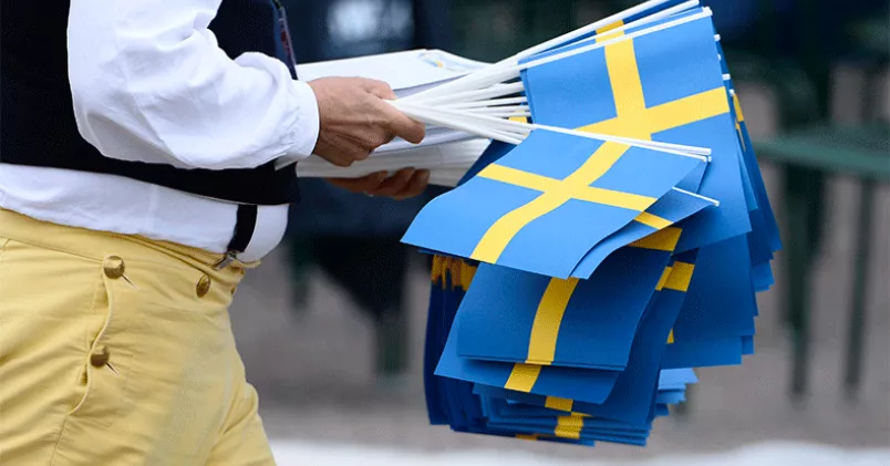 Nationaldag på en lördag. Man iförd folkdräkt bär på svenska flaggor.