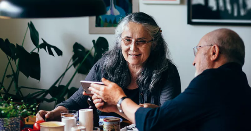 5 400 kronor efter skatt kan det skilja mellan om du går i pension vid 67 i stället för vid 62. Man och kvinna i pensionsålder sitter vid matbord.