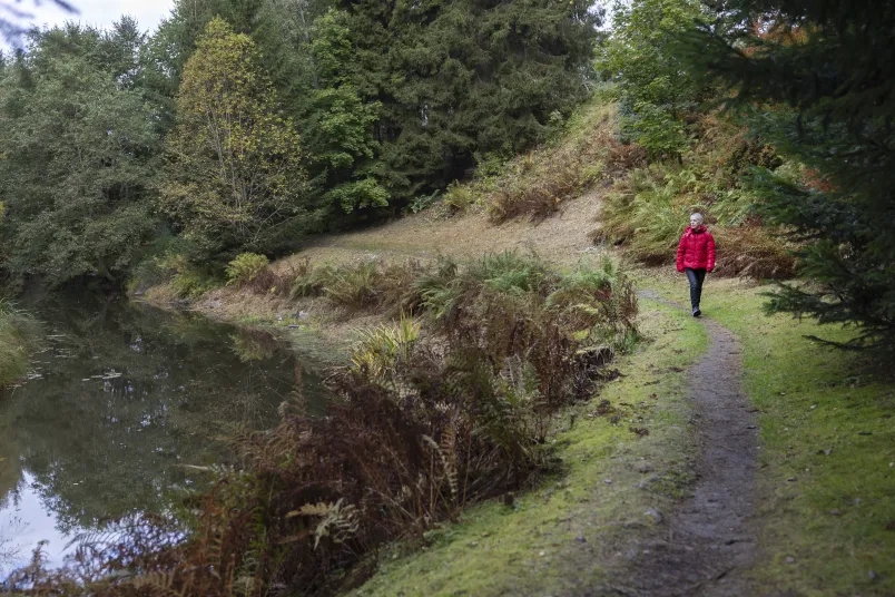 Maria Westin Maria Westin går längs med en älv i röd jacka. Det ser ut som höst med gula och röda löv på träden.