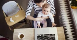 Kvinna med bebis i knät sitter vid dator.