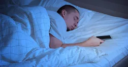 Man ligger och sover med mobilen i handen.