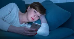 Kvinna ligger i soffan och tittar på sin mobil.