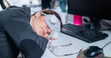Att ta en tupplur på jobbet kan förbättra både koncentrationen och göra dig piggare. Men att sova bort hela arbetsdagen kan stå dig dyrt.. Kvinna iförd sovmask sover med huvudet på skrivbordet.